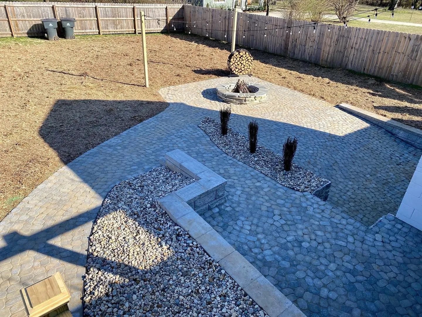 Stone patio with fire pit, gravel border, and string lights