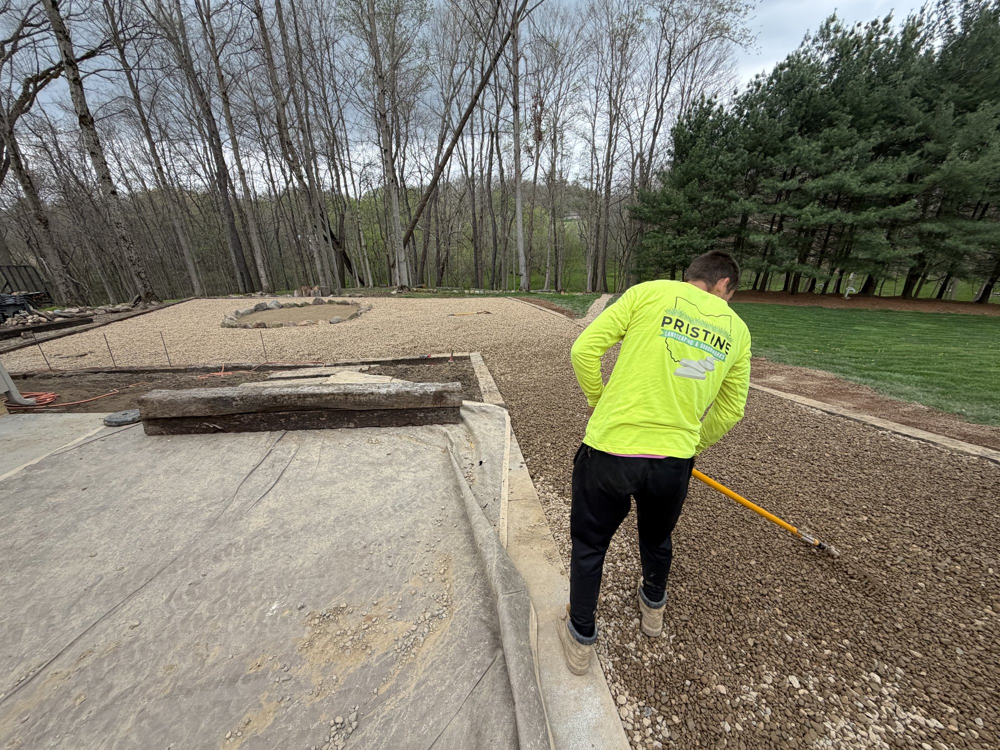 Pristine crew member in branded gear grading a gravel base on a custom build