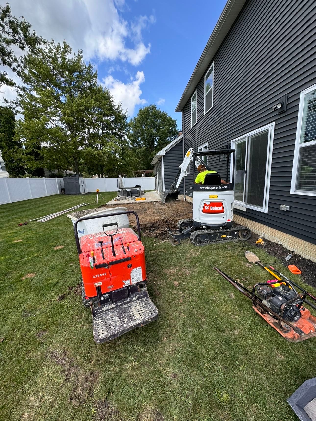 Compact excavator and plate compactor preparing a backyard site