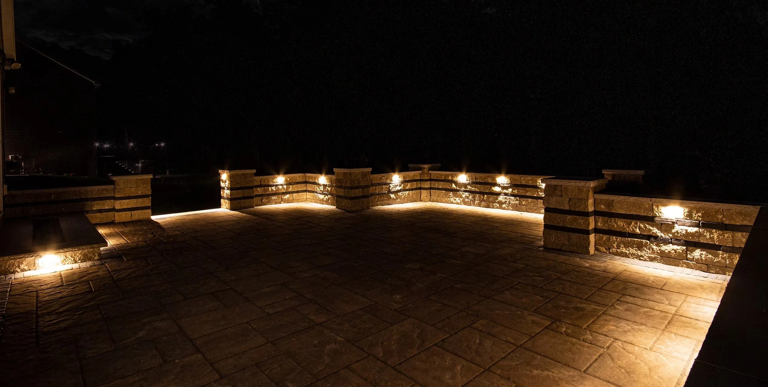 Illuminated paver patio and retaining wall at dusk, built by Pristine Landscaping & Groundworks in Northeast Ohio